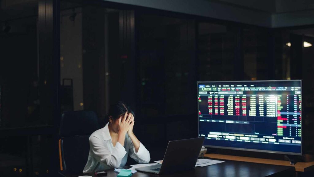 Frustrated trader sitting in front of trading charts at night, representing emotional trading, losses, and the dangers of revenge trading in financial markets.