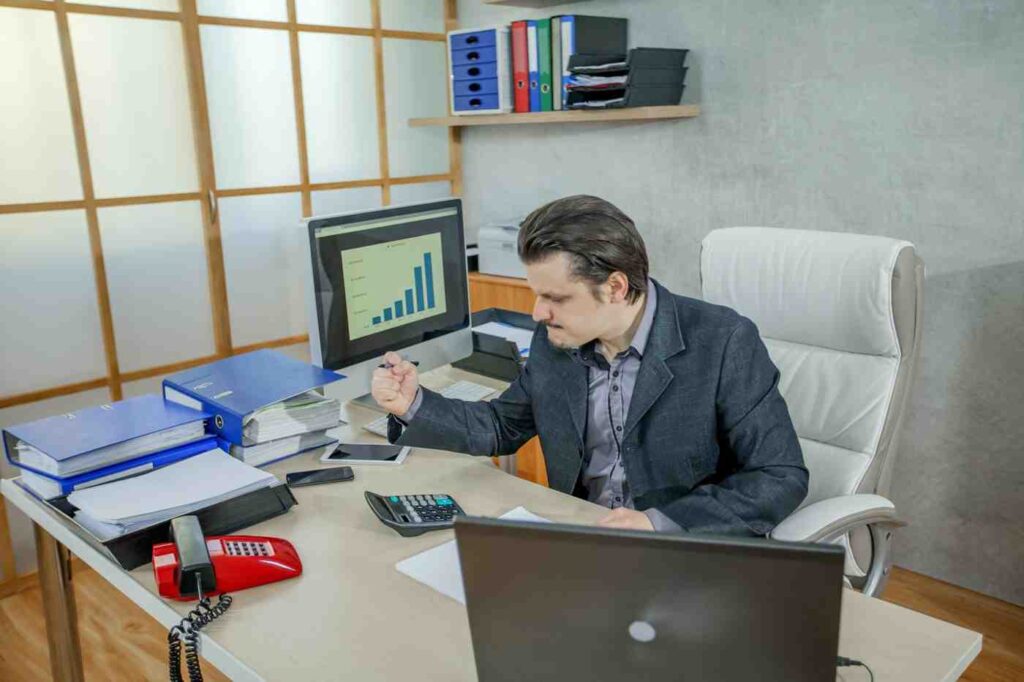 Trader sitting at a desk analyzing charts and financial data while showing frustration caused by emotional trading and overtrading in the market.