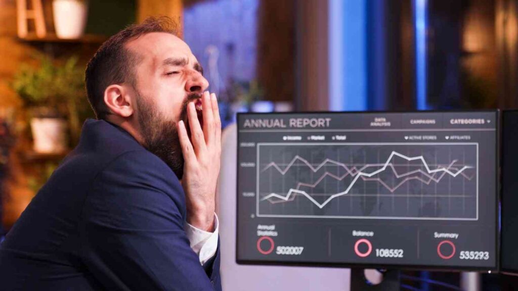 Trader yawning while monitoring market charts on a trading screen, illustrating how disciplined and consistent trading often feels boring compared to emotional and impulsive trading.