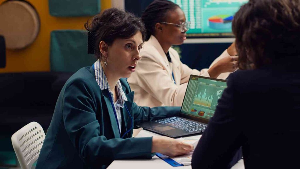 Trader analyzing market data with colleagues while reviewing financial charts, illustrating the sunk cost fallacy in trading where past investments influence decisions instead of current market conditions.