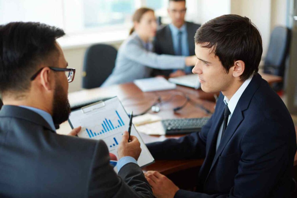 Two traders reviewing financial charts and market data, illustrating anchoring bias in trading where decisions are influenced by previous price levels instead of current market conditions.