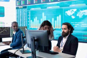 Trader analyzing financial charts with a colleague, illustrating how anchoring bias appears in trading when traders base their decisions on entry prices, previous highs, or outdated price levels instead of current market conditions.